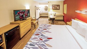 A hotel room with a bed, a desk with a television, a chair, a small table with a lamp, and a bathroom visible through an open door. - Red Roof Inn Charleston West - Hurricane, WV (Hurricane)