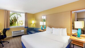 A hotel room with a large bed, a desk, a chair, a desk lamp, a nightstand, and a window with curtains. - La Quinta Inn & Suites by Wyndham Sarasota Downtown (Sarasota)