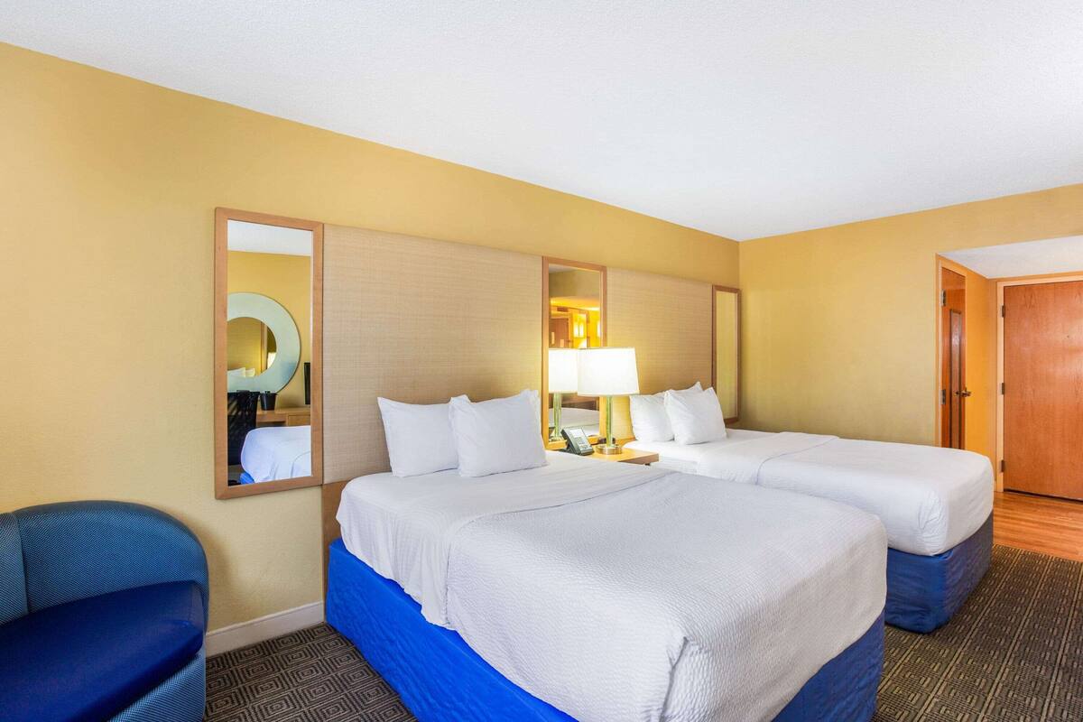 Ein Hotelzimmer mit zwei Betten, einem Schreibtisch, einem Stuhl und einem Spiegel.