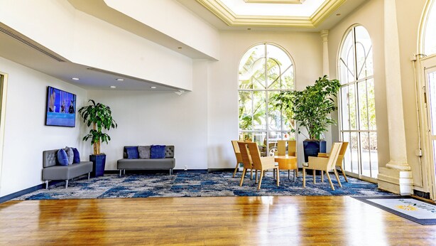 A spacious lobby with a wooden floor, two sofas, a dining area with chairs, large windows, and potted plants. - La Quinta Inn & Suites by Wyndham Sarasota Downtown (Sarasota)