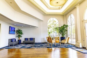 A spacious lobby with a wooden floor, two sofas, a dining area with chairs, large windows, and potted plants. - La Quinta Inn & Suites by Wyndham Sarasota Downtown (Sarasota)