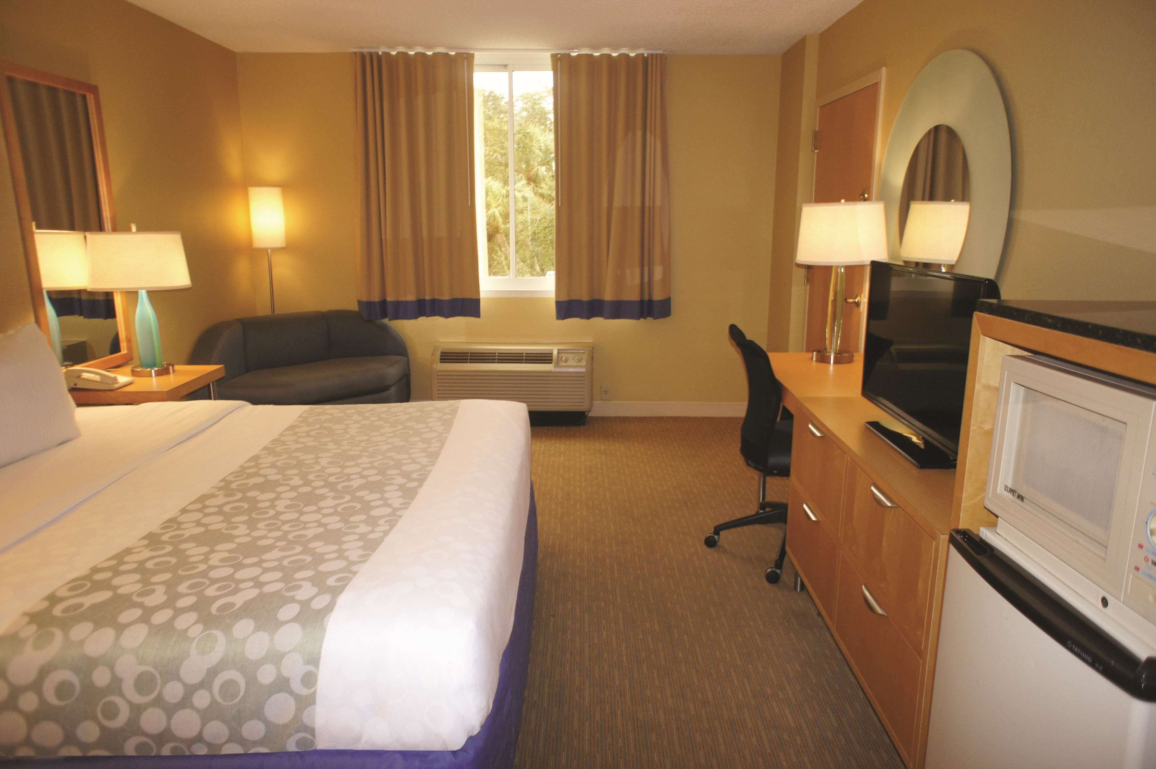 Habitación de hotel con cama, escritorio, televisor, microondas y ventana con cortinas.