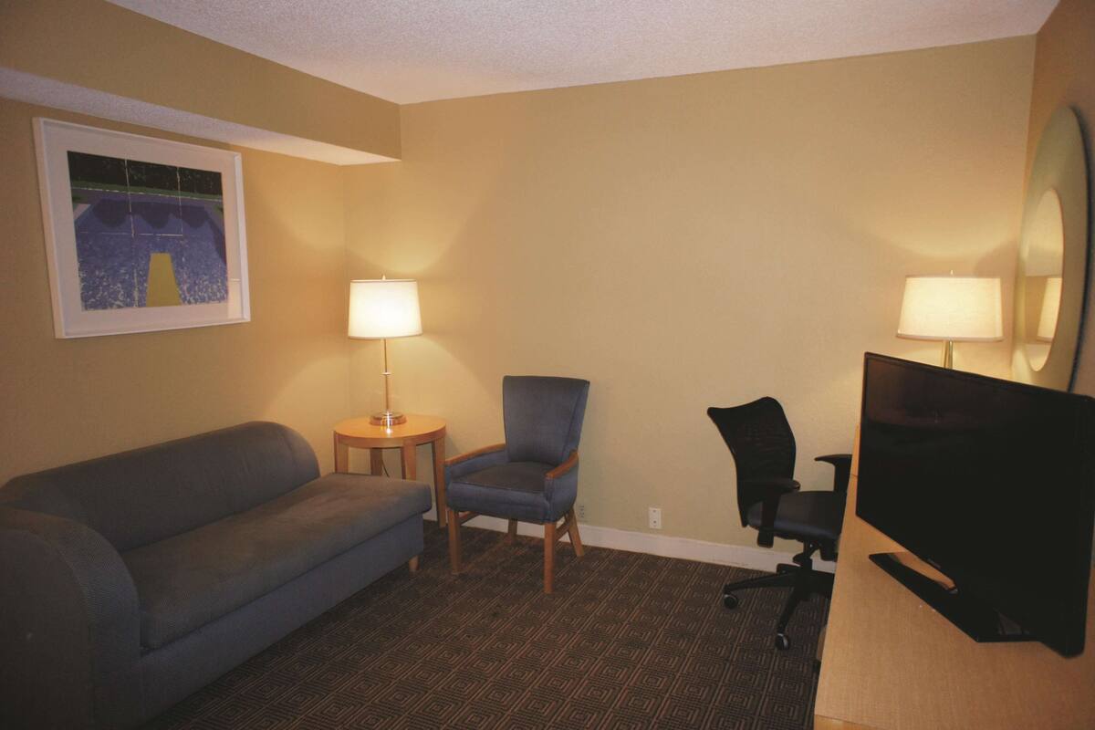Ein Hotelzimmer mit einer Couch, einem Sessel, einem Schreibtisch mit Fernseher und zwei Lampen.