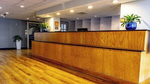 A reception desk with a wooden finish, a potted plant, and a computer monitor. - La Quinta Inn & Suites by Wyndham Sarasota Downtown (Sarasota)