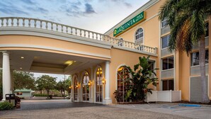 A hotel entrance with a covered walkway, palm trees, and a sign reading "La Quinta Inn Suites". - La Quinta Inn & Suites by Wyndham Sarasota Downtown (Sarasota)