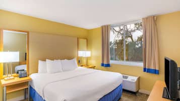 A hotel room with a large bed, bedside lamps, a desk with a telephone, a television, and a window with curtains.