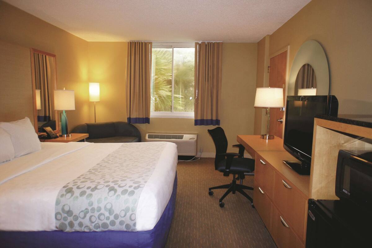Ein Hotelzimmer mit einem großen Bett, einem Schreibtisch mit Fernseher, einem Sessel und einer Schreibtischlampe.