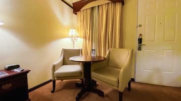 A hotel room with a round table, two armchairs, a lamp, a door, and a small desk with a telephone.