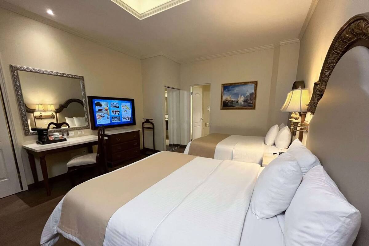 A hotel room with two beds, a desk with a computer, a TV, and a painting on the wall.