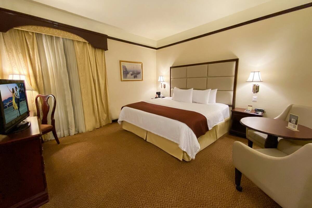 A hotel room with a large bed, a desk, a chair, a television, and a window with curtains.
