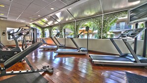 Un gimnasio con cintas de correr, máquinas de pesas y suelo de madera.