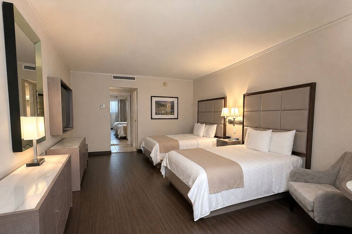 A hotel room with two beds, a desk, a chair, a mirror, and a framed picture on the wall.