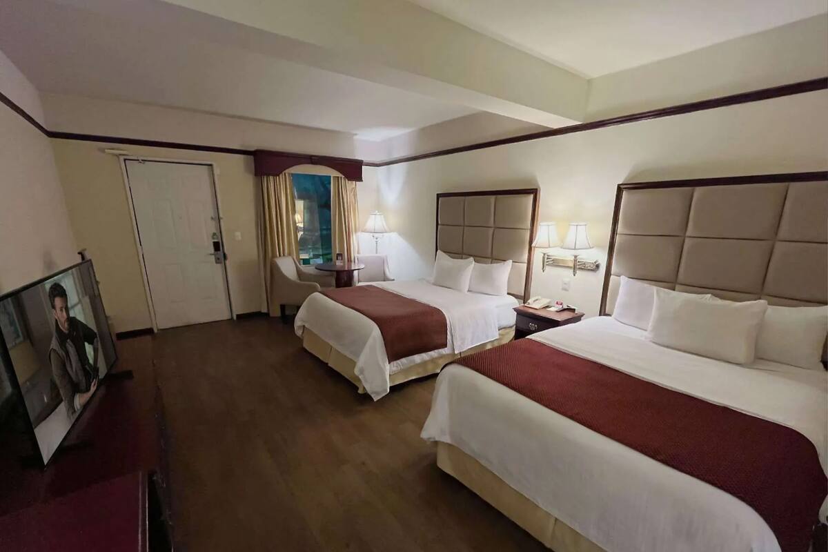 A hotel room with two beds, a desk, a chair, a TV, and a window with curtains.