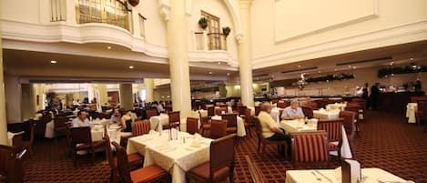A spacious restaurant with multiple dining areas, high ceilings, and decorative plants.