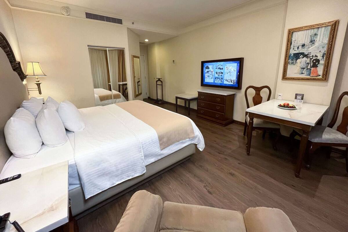 A hotel room with a bed, a TV, a dining table, and a chair.