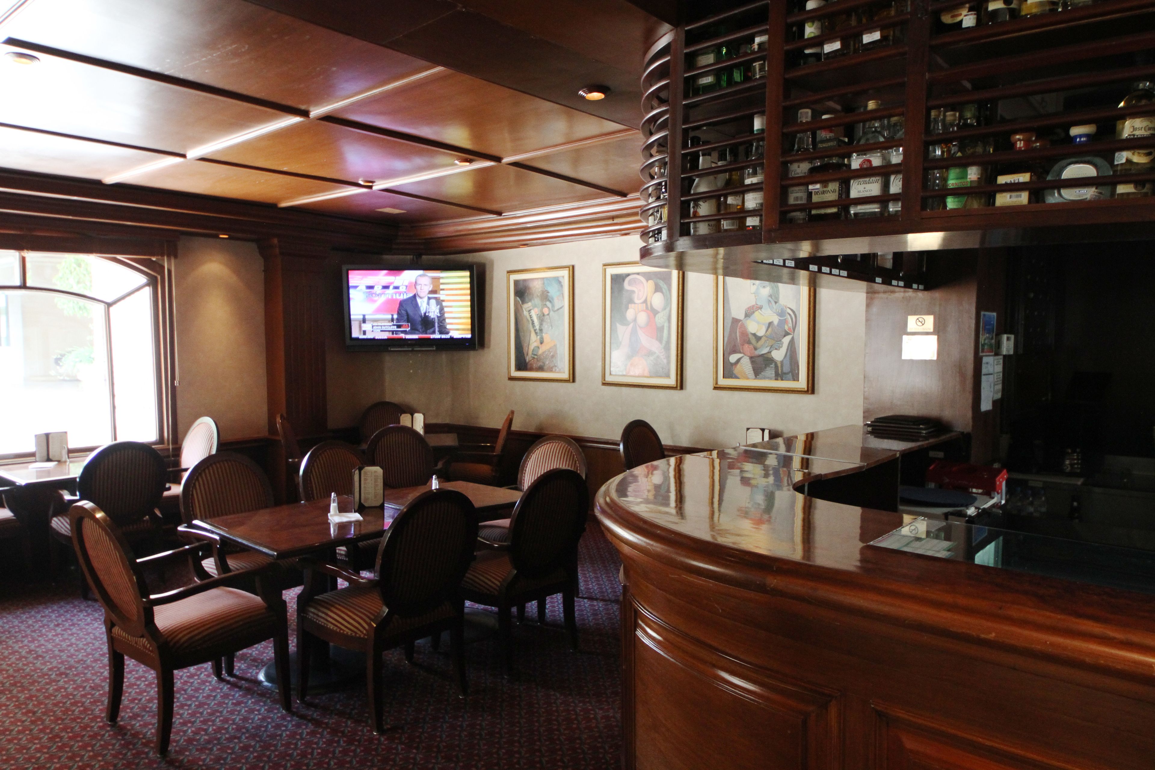 Una zona de bar con muebles de madera, un televisor montado en la pared y cuadros enmarcados.