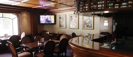 Una zona de bar con muebles de madera, un televisor montado en la pared y cuadros enmarcados.