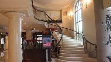 Una majestuosa escalera con diseño curvo, un mostrador de recepción con un cartel de bienvenida y un amplio ventanal que proporciona luz natural.