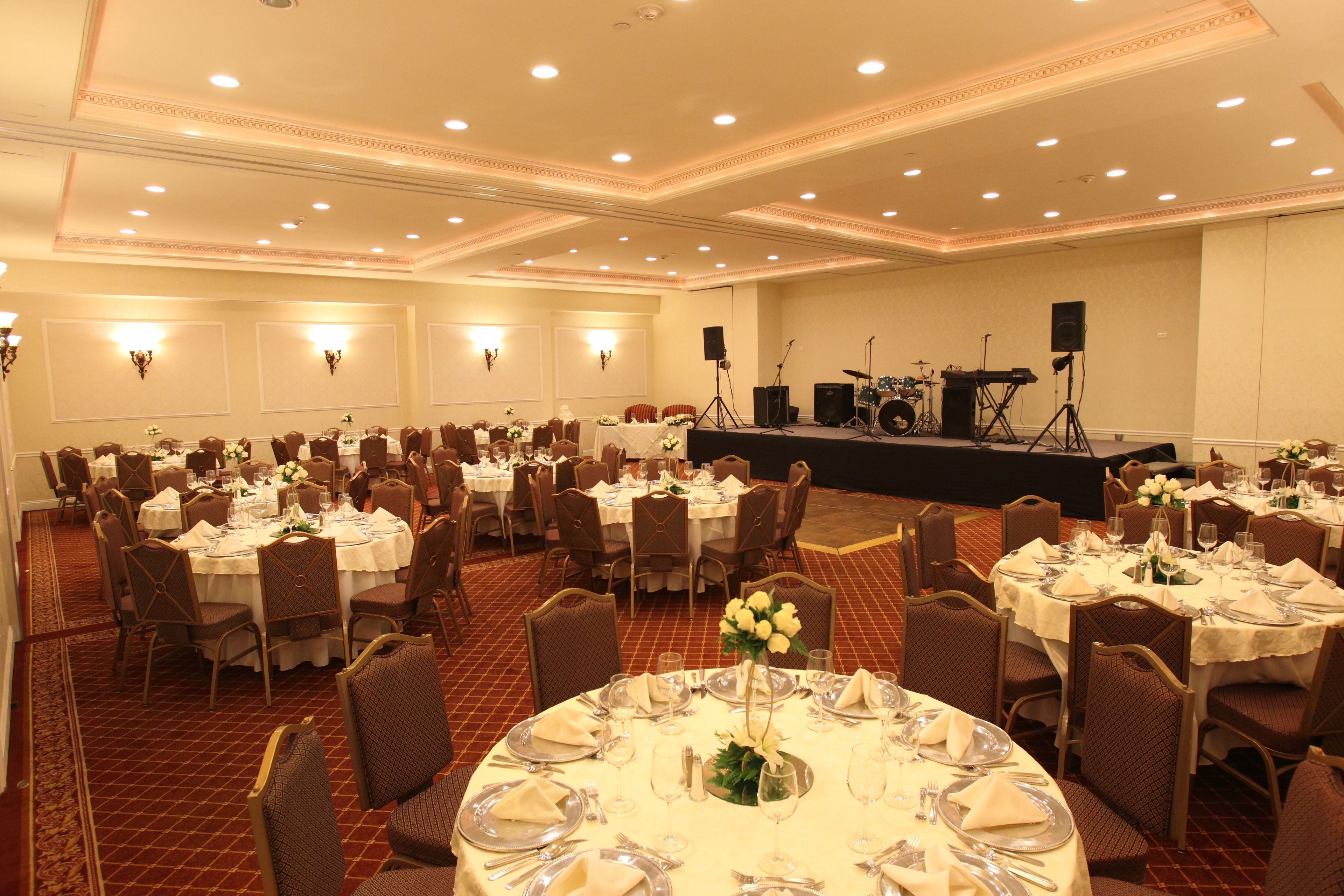 Un salón de banquetes con mesas redondas dispuestas para comer, un escenario con equipo musical y un suelo alfombrado.