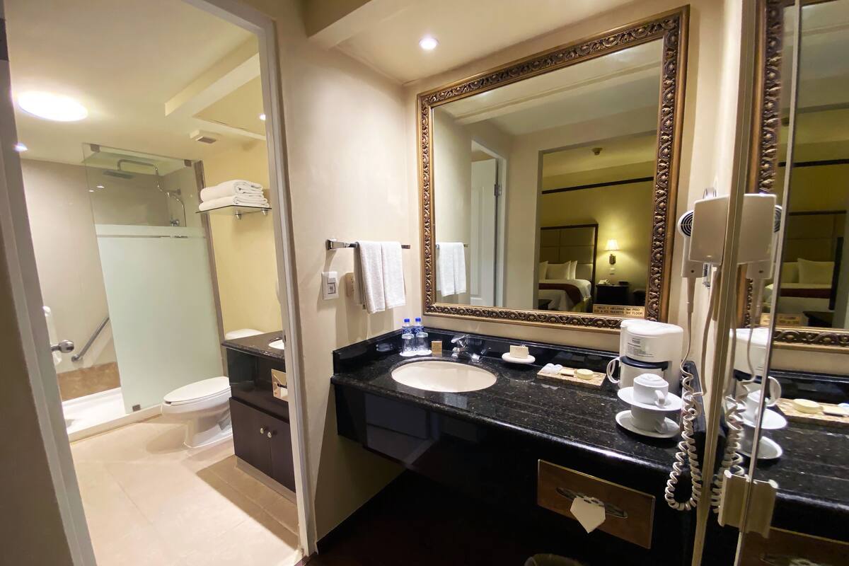 A hotel bathroom with a large mirror, a sink, a shower, and a hairdryer.