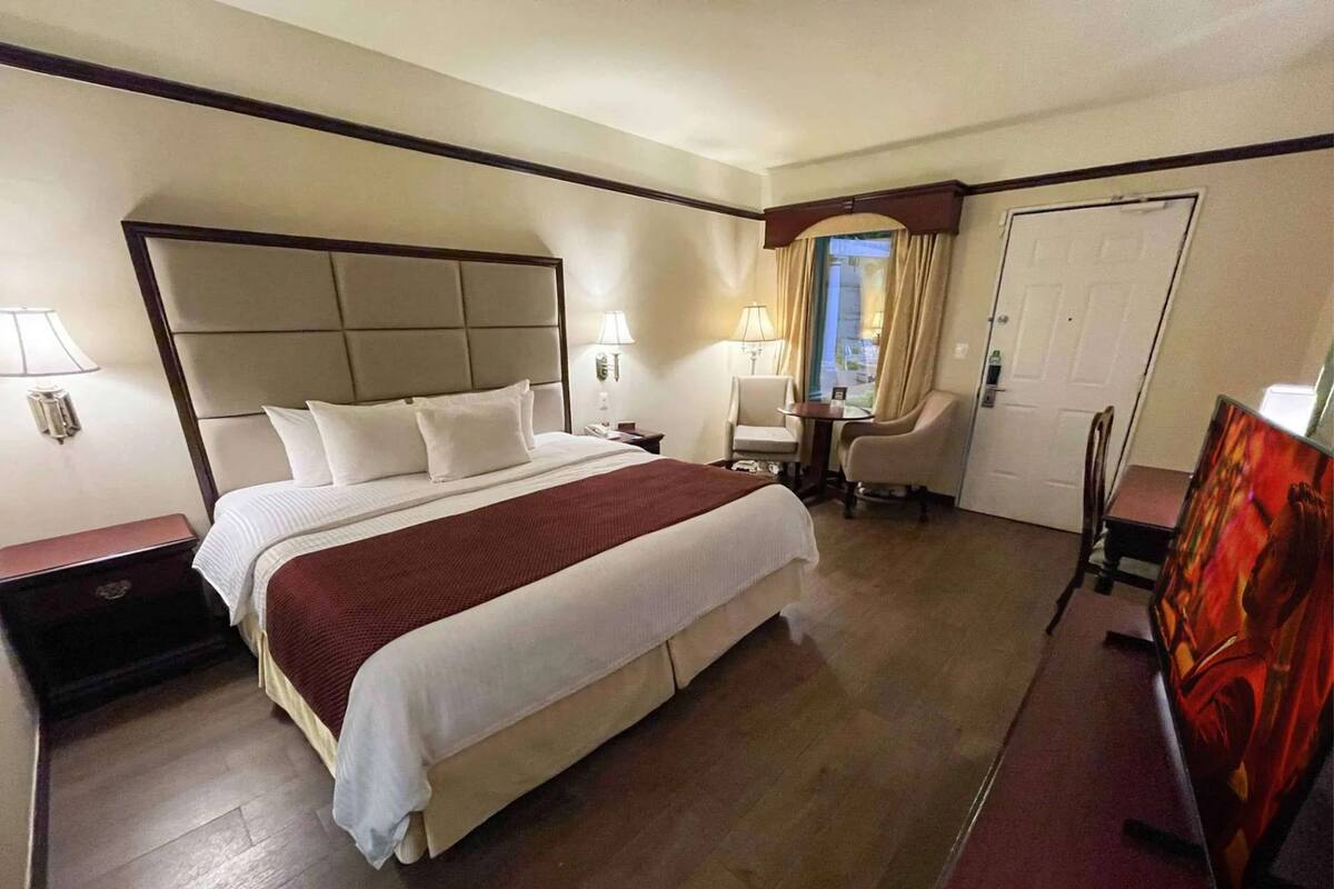 A hotel room with a large bed, bedside tables, a desk, a chair, and a door.