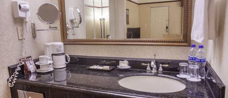 A hotel bathroom with a sink, mirror, hair dryer, and coffee maker.