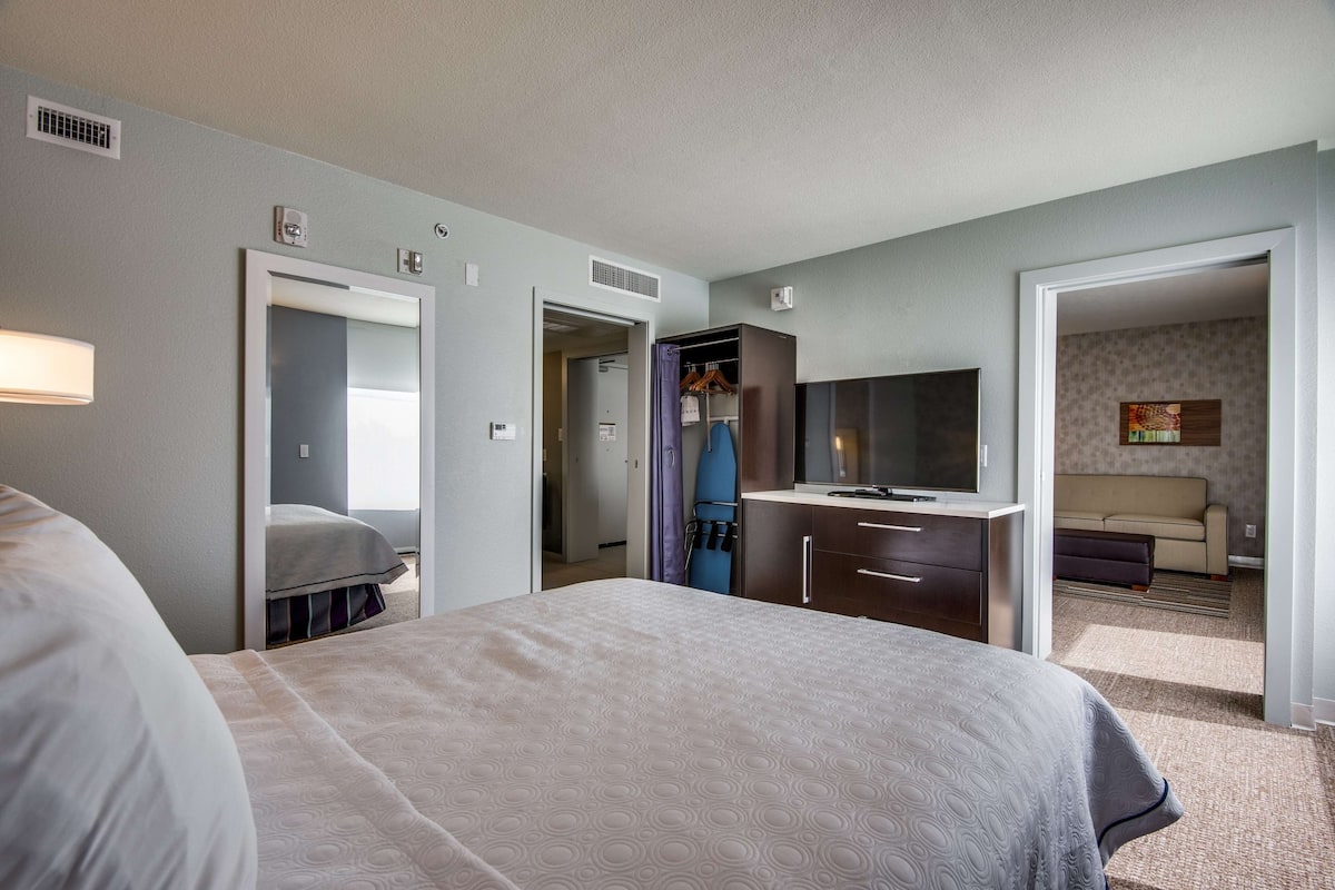 Una habitación de hotel con cama, escritorio, espejo, armario y televisor.