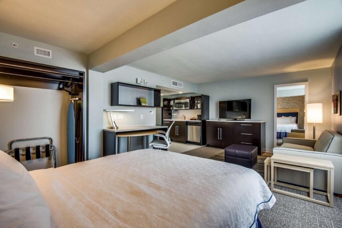 A hotel room with a bed, a desk, a kitchenette, a TV, and a seating area.