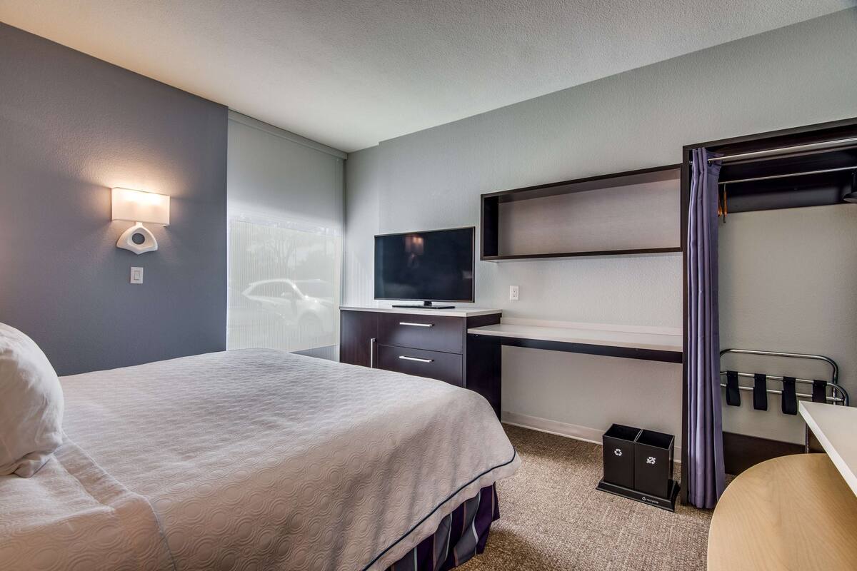 Habitación de hotel con cama, escritorio con televisor, armario y zona de baño.