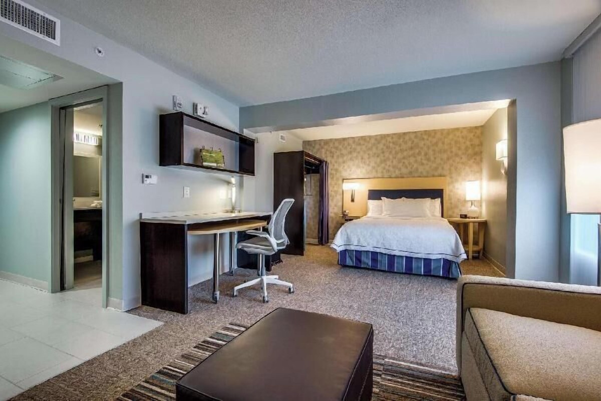 A hotel room with a bed, desk, chair, and a small seating area.
