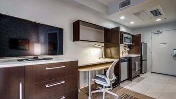 A modern kitchen with a built-in microwave, a large flat-screen TV, and a white desk with a chair.