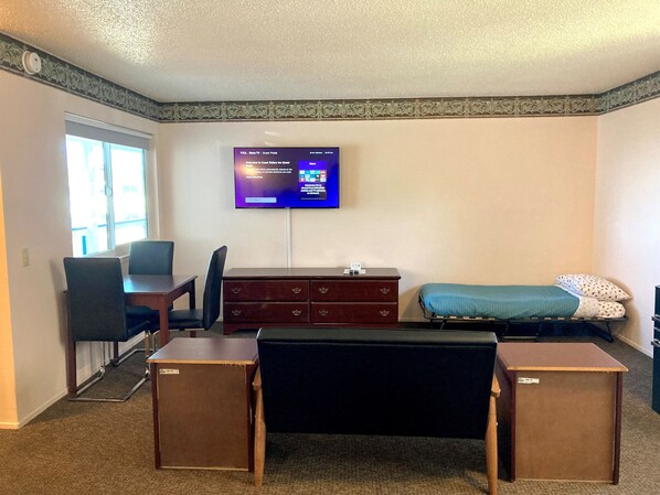 A hotel room with a desk, chair, TV, bed, and dresser.