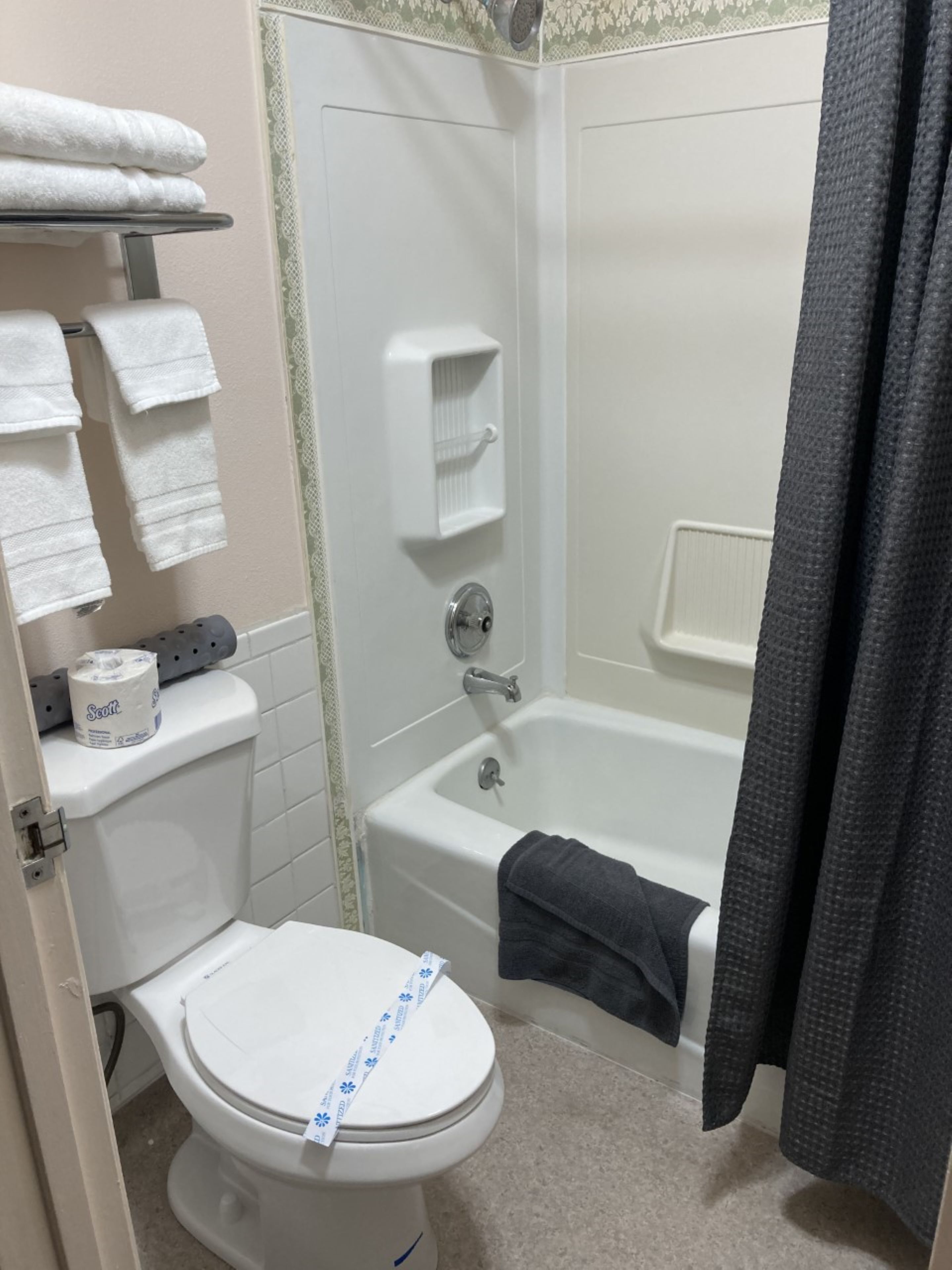 A bathroom with a toilet, a shower, and a bathtub. There are towels on a rack and a toilet paper roll on the toilet.