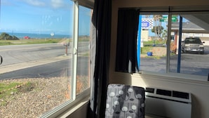 Quarto com uma janela grande que dá para a estrada e o oceano, uma cadeira e um termostato.