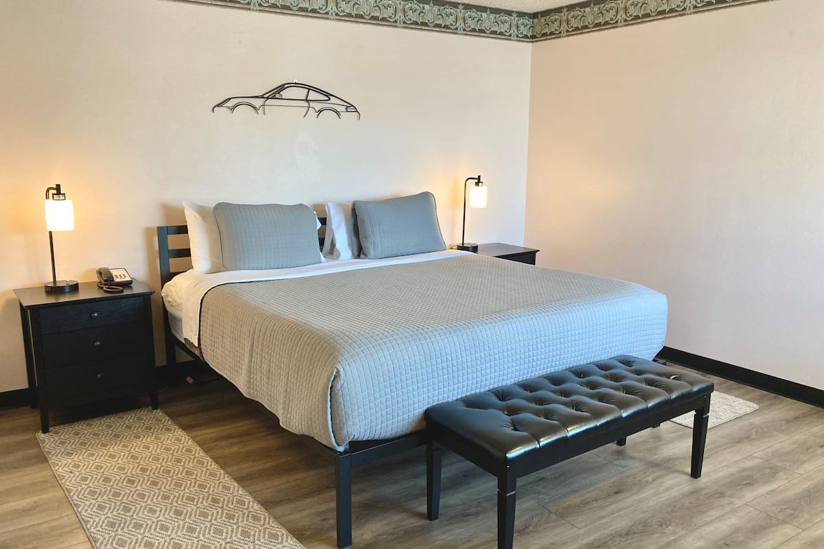 Un dormitorio ordenado con una cama, dos mesitas de noche con lámparas, un banco y una alfombra estampada.