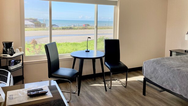 Quarto de hotel com uma cama, duas cadeiras, uma pequena mesa com cafeteira e janela com vista para a praia e oceano.