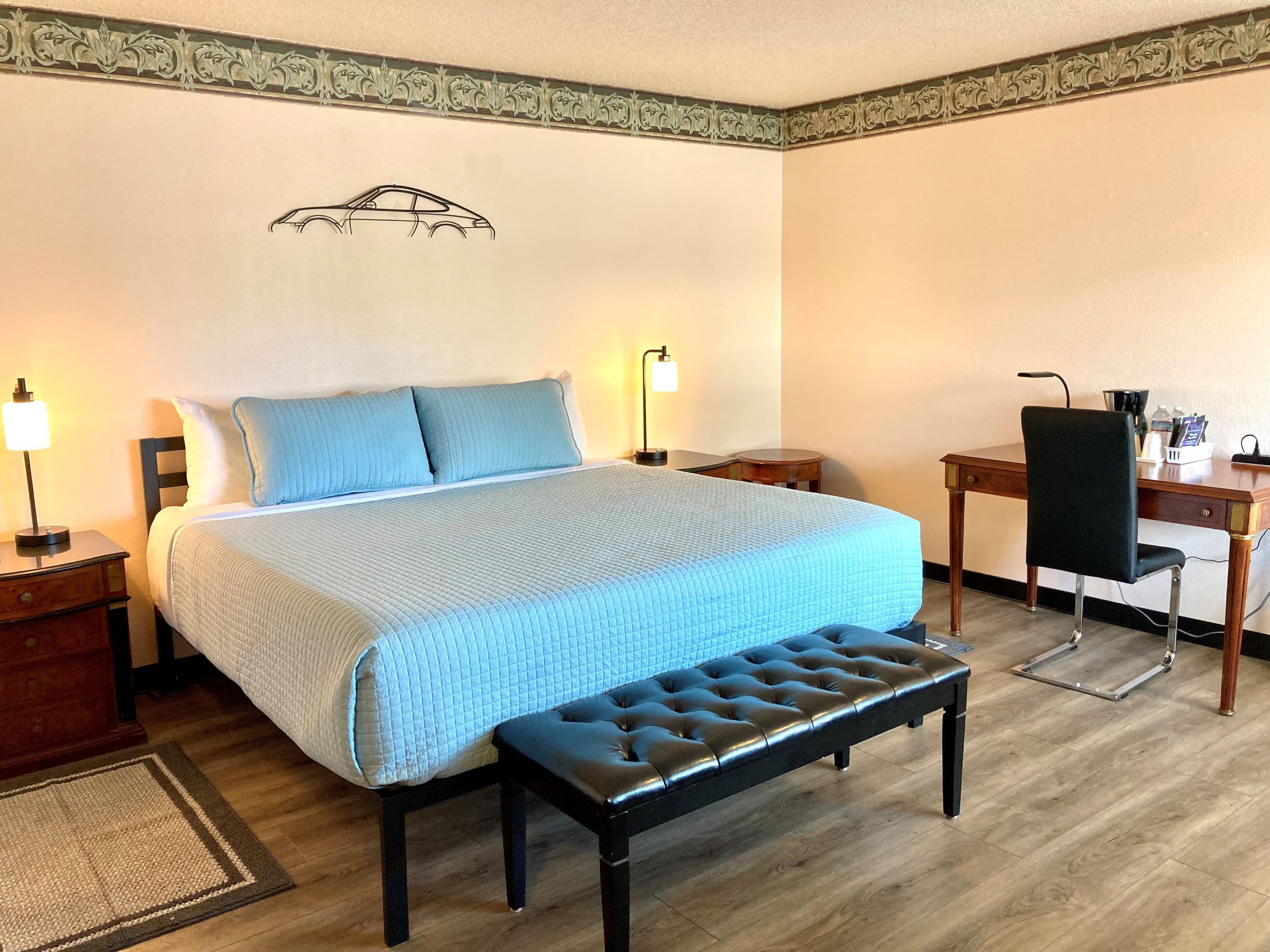 Habitación de hotel con cama, mesitas de noche, escritorio, una silla y una obra de arte colgada en la pared.