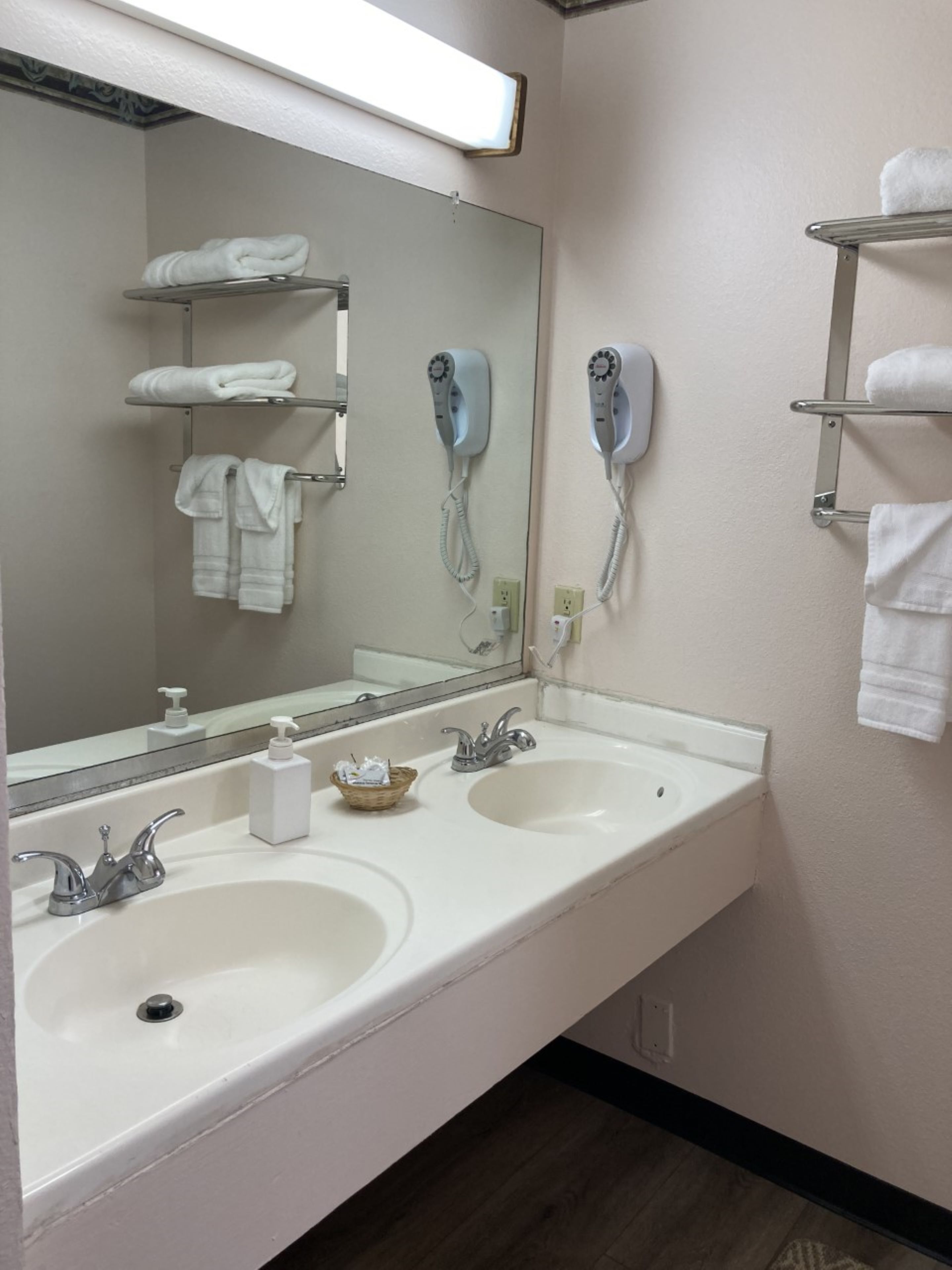 A bathroom with two sinks, a large mirror, and a hairdryer mounted on the wall.