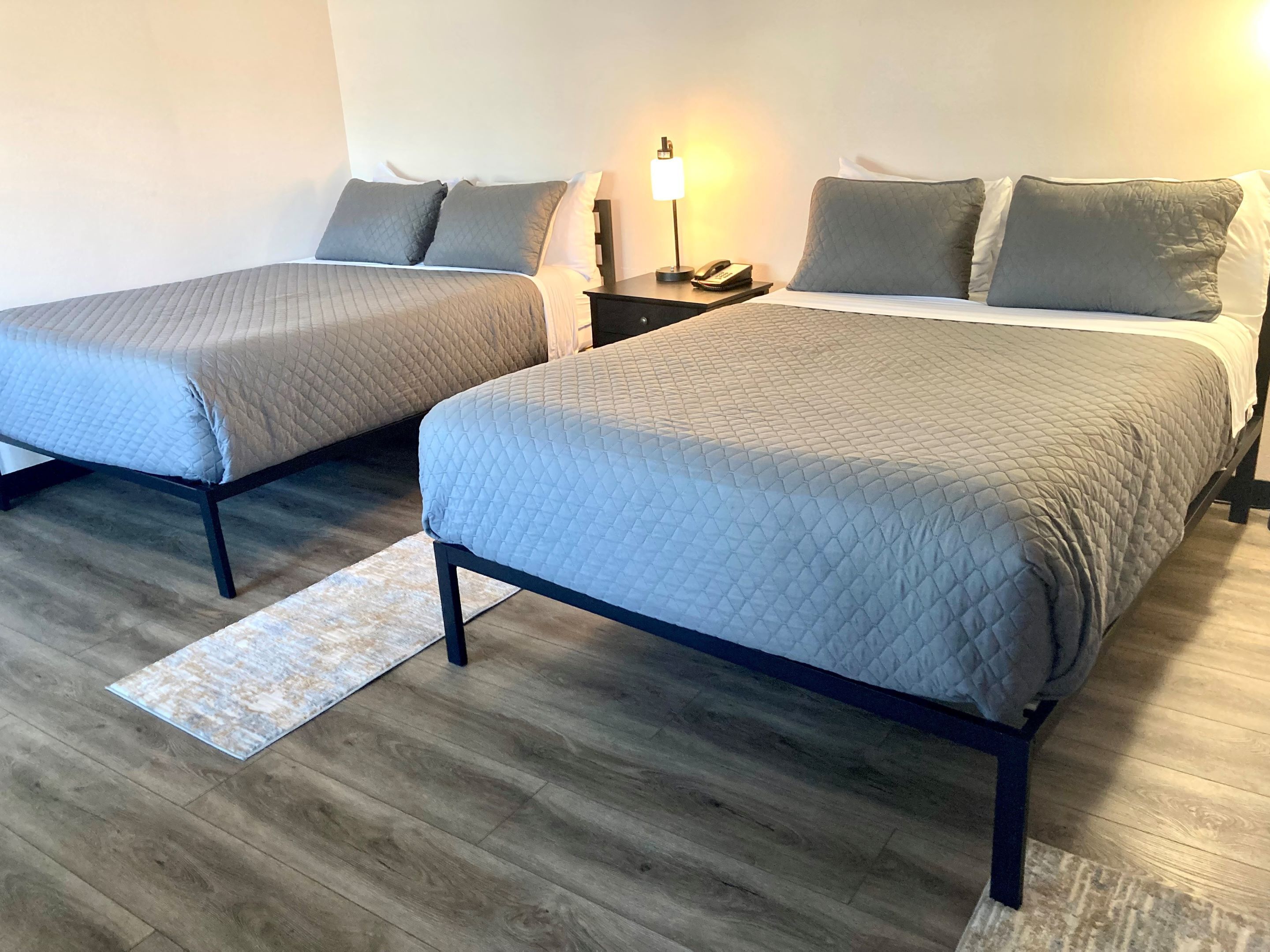 Een hotelkamer met twee bedden, een nachtkastje met een lamp en een houten vloer.