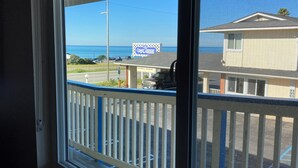 Vista pela janela com corrimão branco, sobre uma rua com o letreiro 'Coast Riders' e um edifício com varanda.