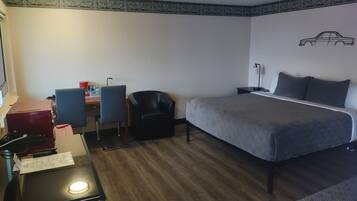 Una camera d'albergo con un letto, una scrivania, sedie e un muro con un disegno di automobile.