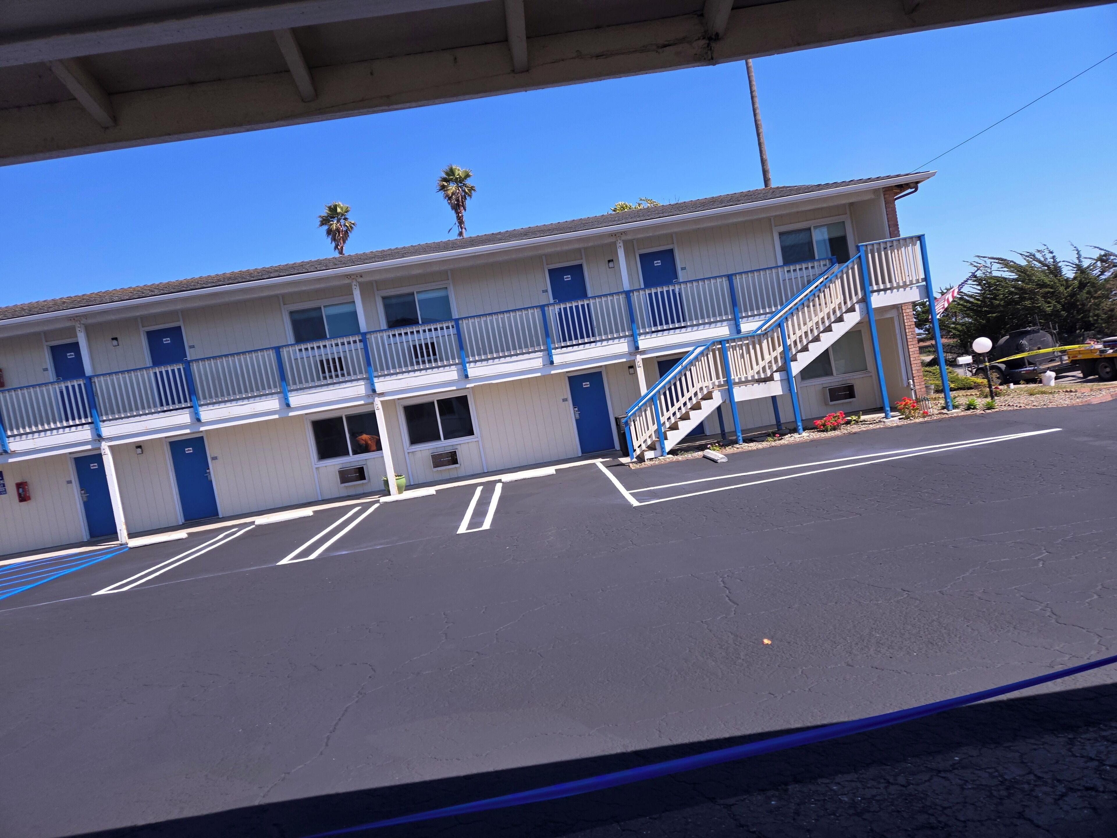 Un motel con una estructura de dos pisos, barandillas azules y un estacionamiento.
