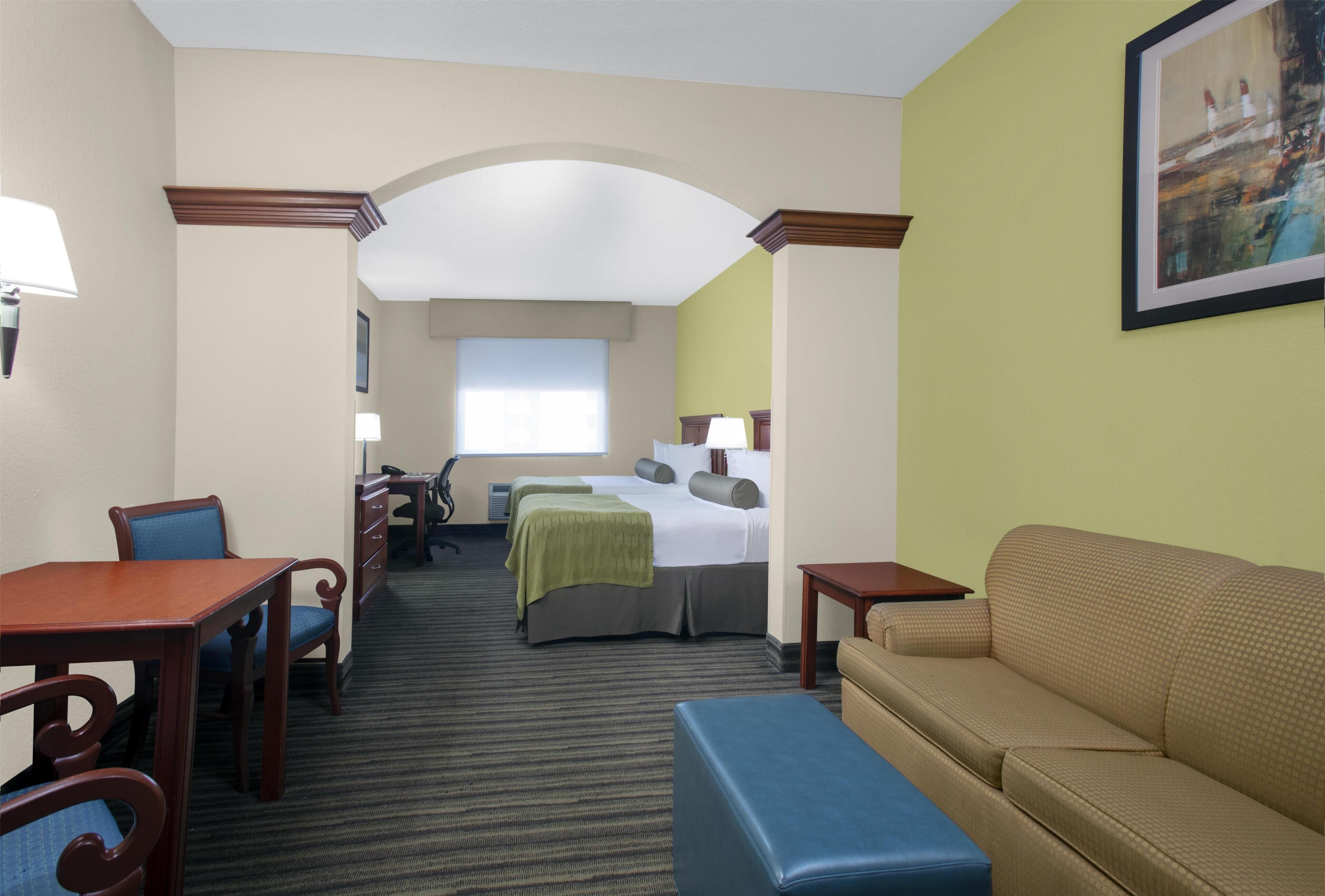 A hotel room with a bed, a desk, a chair, a sofa, and a painting on the wall.