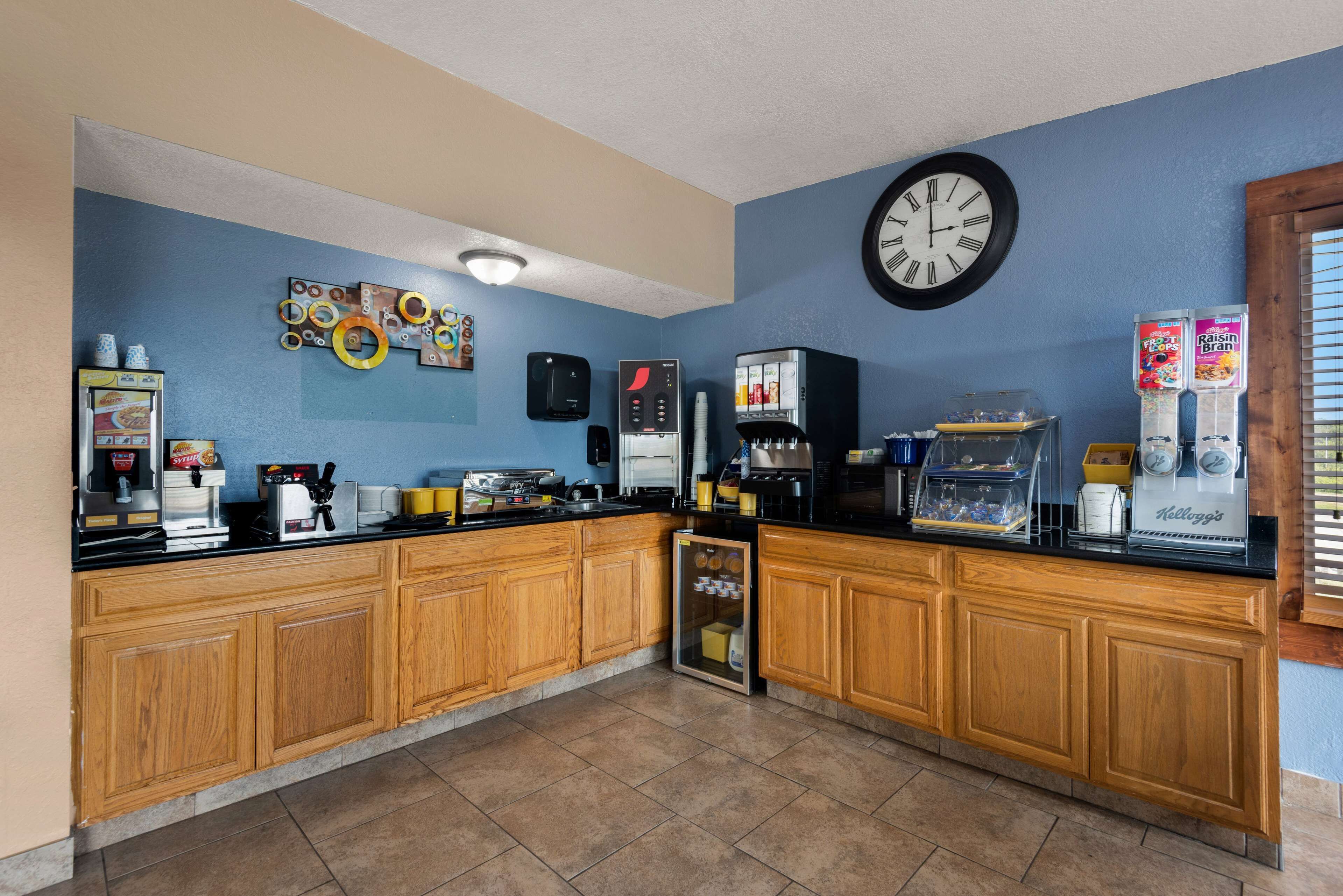 Une cuisine avec des meubles de rangement en bois, une machine à café, un réfrigérateur et une horloge au mur.