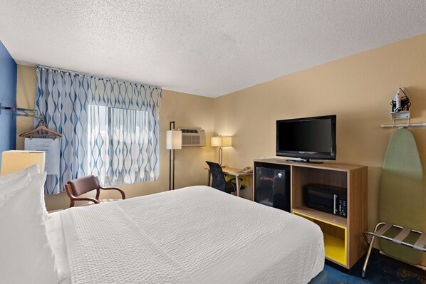 A hotel room with a large bed, a desk with a chair, a television, a microwave, and a window with curtains.