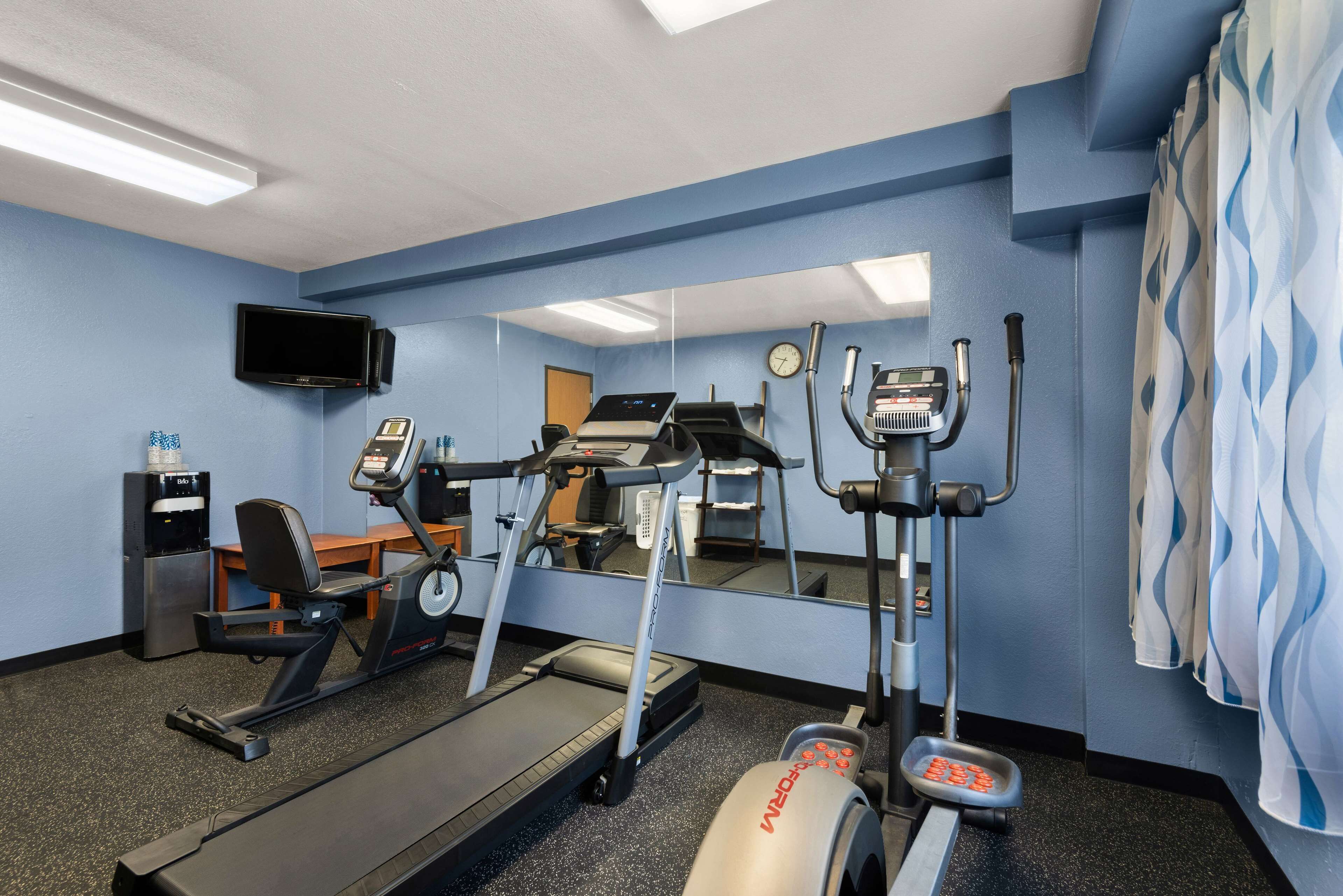 Un gimnasio con equipo de cardio, un espejo, un televisor y un dispensador de agua.