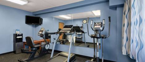 Un gimnasio con equipo de cardio, un espejo, un televisor y un dispensador de agua.