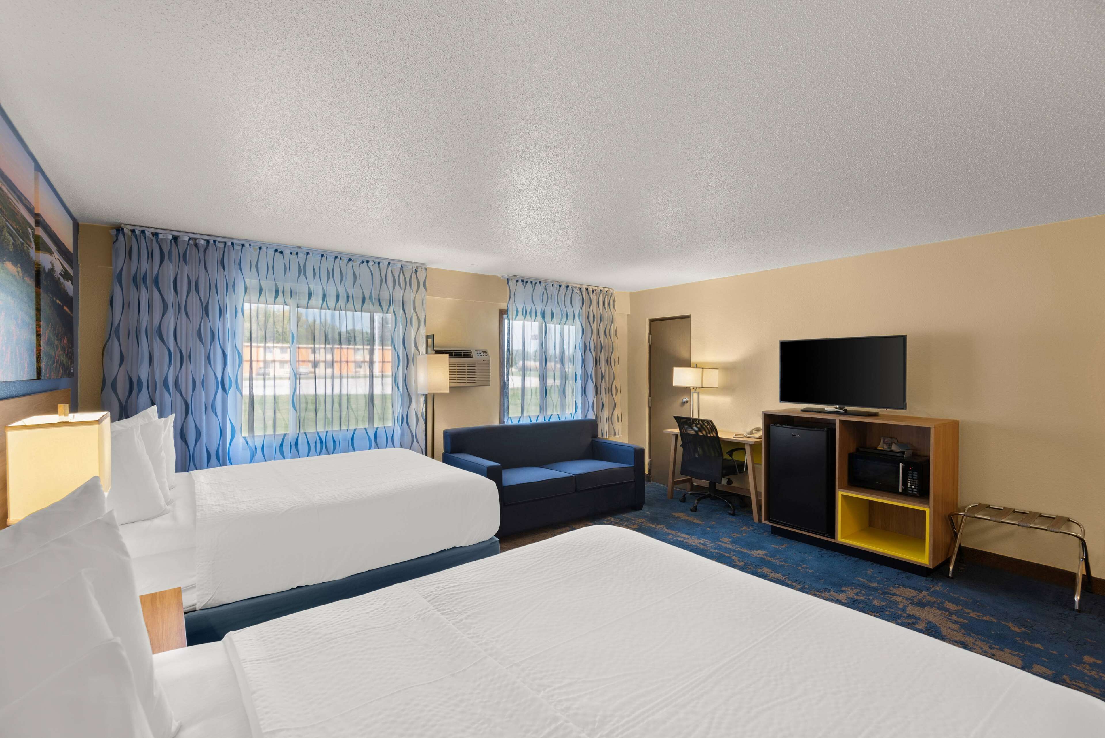 A hotel room with a large bed, a sofa, a desk, a television, and a minibar.