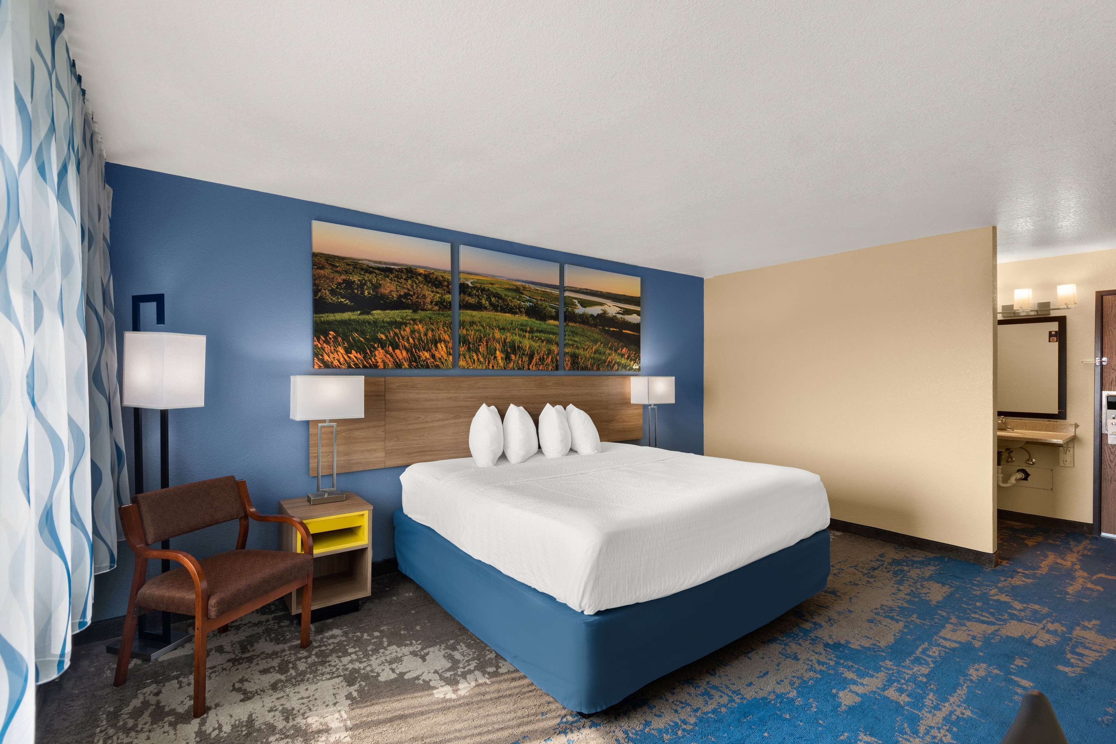 A hotel room with a large bed, a chair, a desk, and a painting on the wall.
