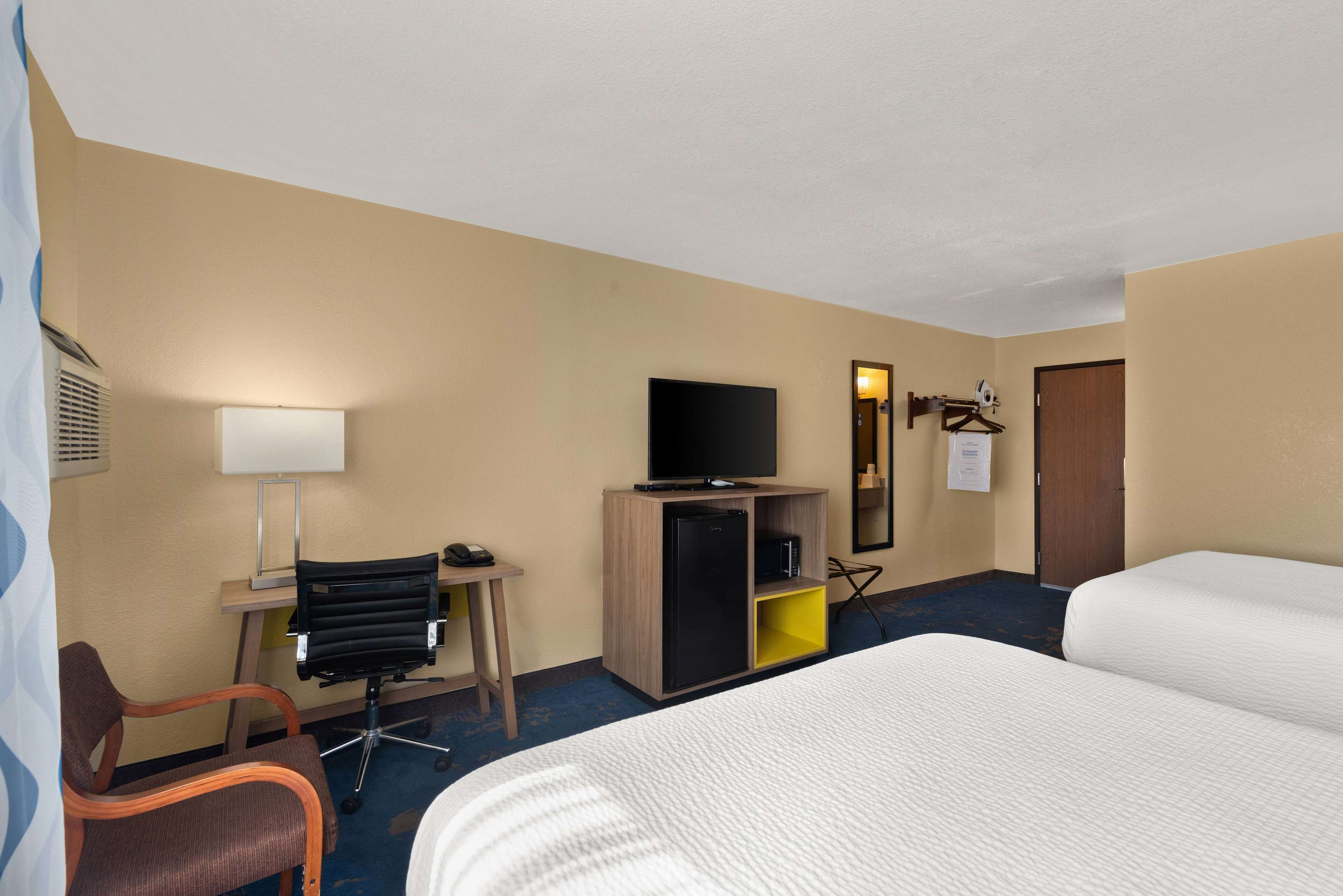 A hotel room with a bed, a desk with a computer, a television, and a small refrigerator.